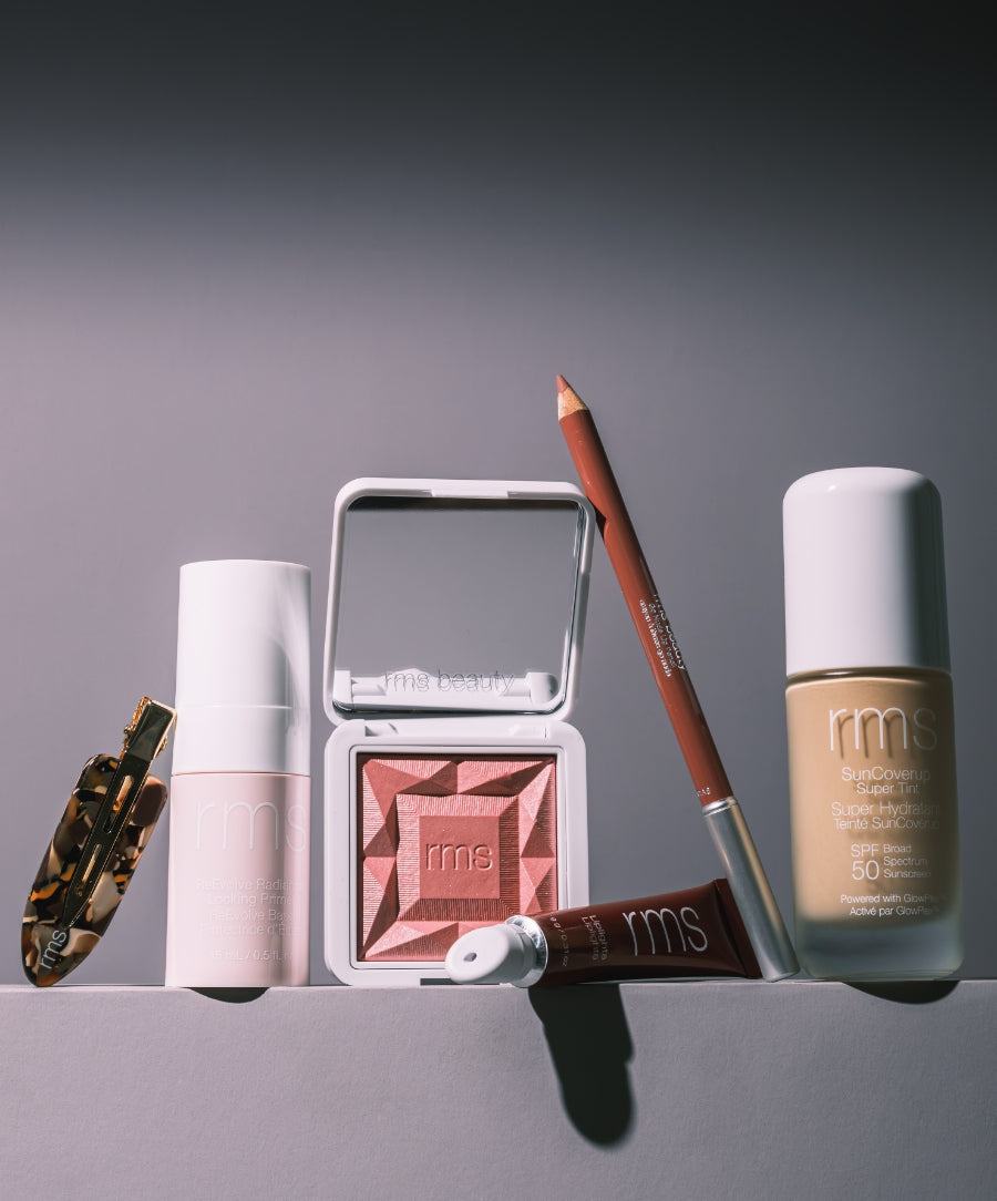 RMS Discovery Kit featuring a collection of clean beauty products including a tinted moisturizer with SPF, cream blush, lip and cheek tint, lip liner, and a tortoiseshell hair clip arranged on a light surface.