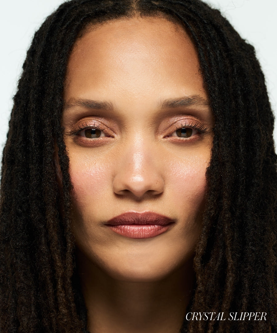 Close-up of a woman with natural dreadlocks wearing Lip2Cheek makeup in a soft, neutral shade highlighting her lips and cheeks with a radiant, clean beauty finish.