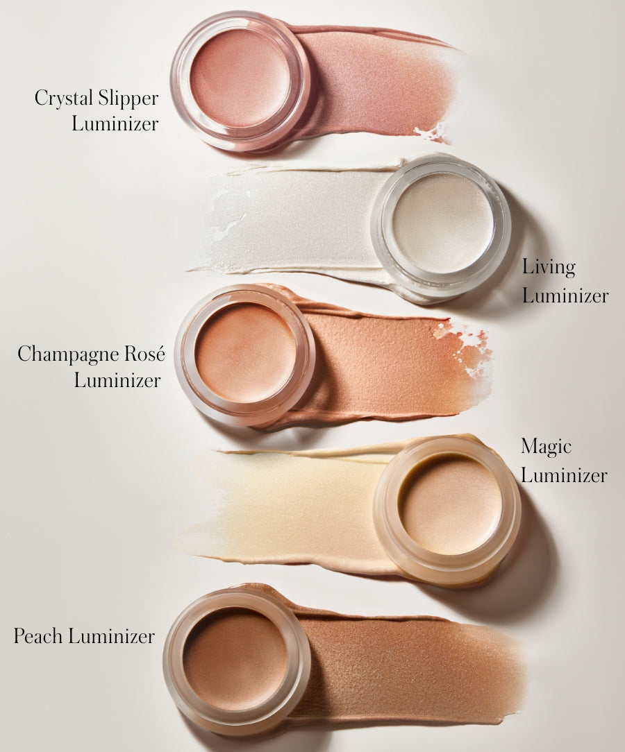 Collection of five Luminizer cream highlighters in glass jars with smooth swatches in soft neutral, pink, white, peach, and bronze shades on a light background, showcasing clean beauty makeup.