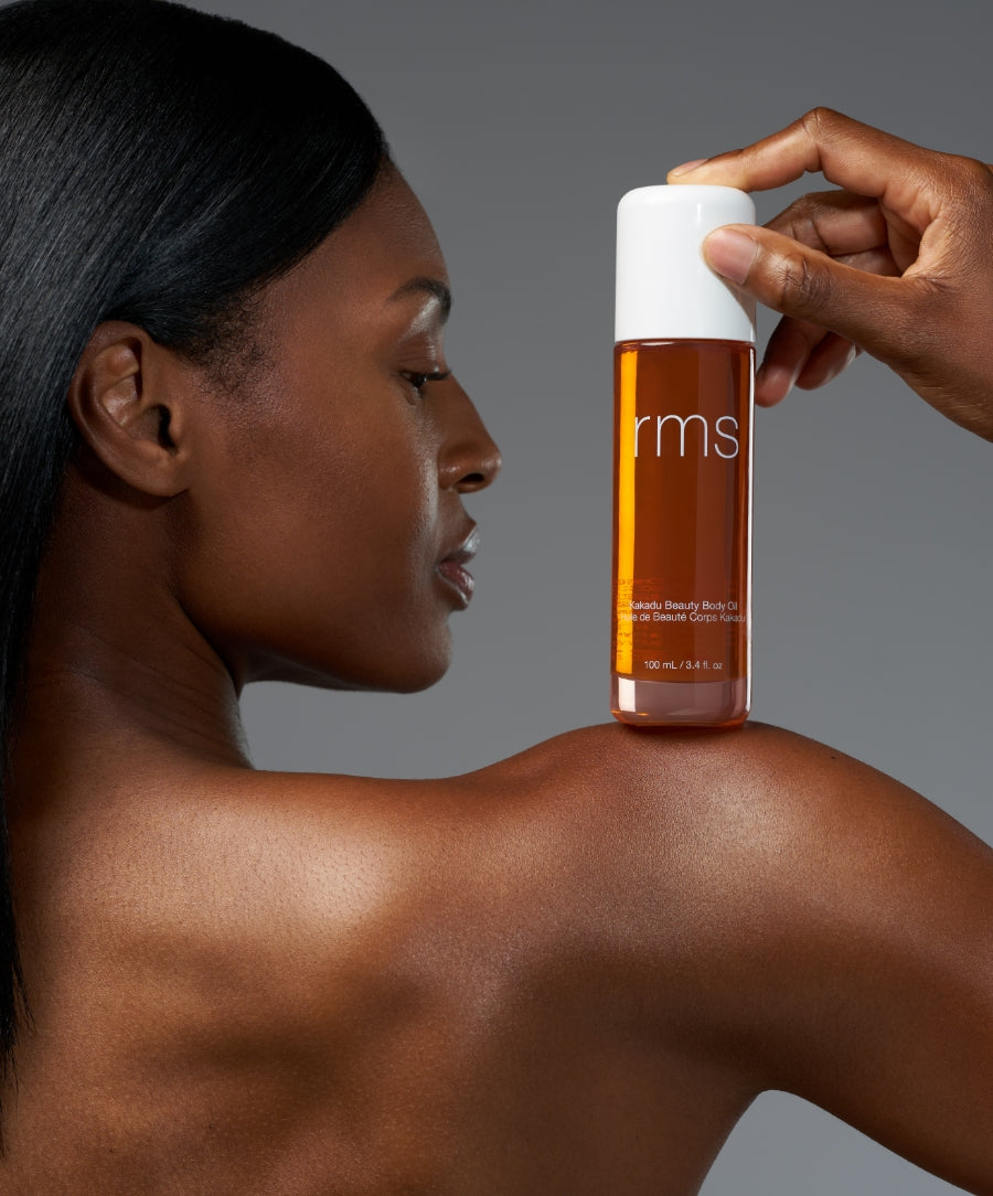 A close-up of a person holding a bottle of Kakadu Body Oil near their shoulder, showcasing smooth, glowing skin and highlighting natural body care with clean, sustainable ingredients.
