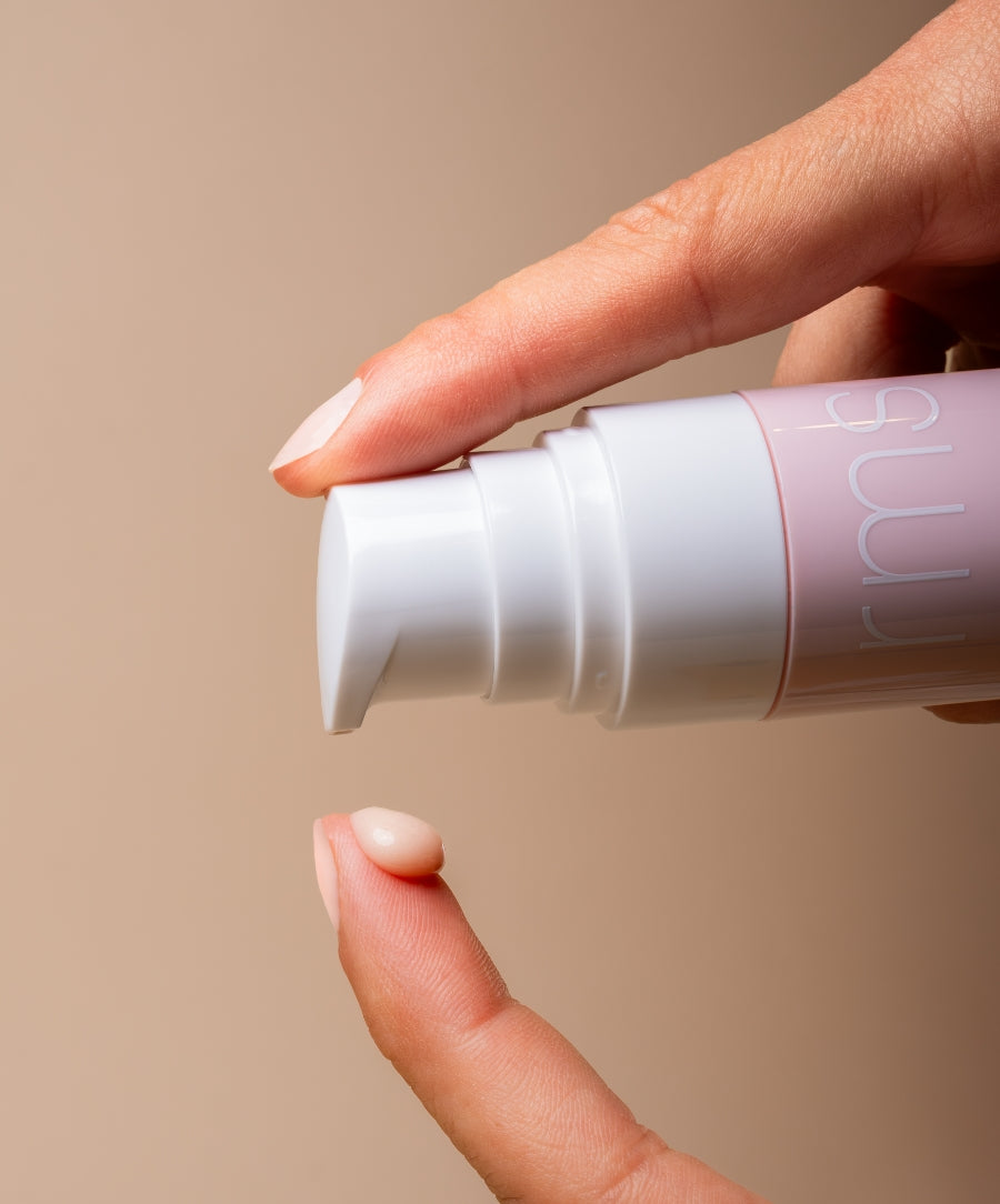 Close-up of a hand dispensing a small amount of ReEvolve Radiance Locking Primer from a white and pink pump bottle, showcasing the smooth texture of the clean beauty product.
