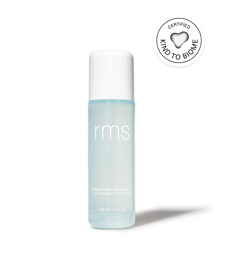 A transparent bottle with white cap containing light blue Kakadu Clean Cleansing Gel by RMS, shown with a certified Kind to Biome symbol highlighting clean beauty and sustainable packaging.