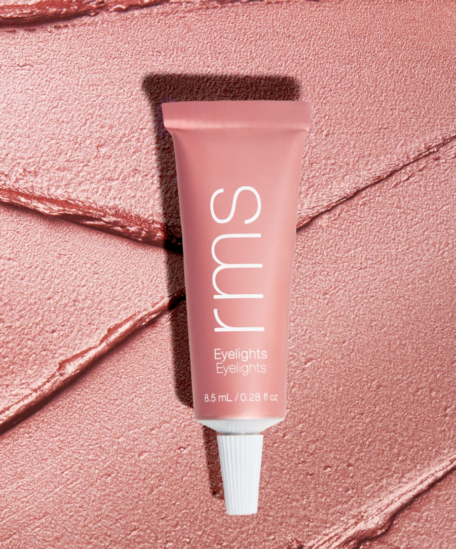Tube of Eyelights Cream Eyeshadow in a soft pink shade with a creamy, shimmery texture background, highlighting clean beauty and natural ingredients.