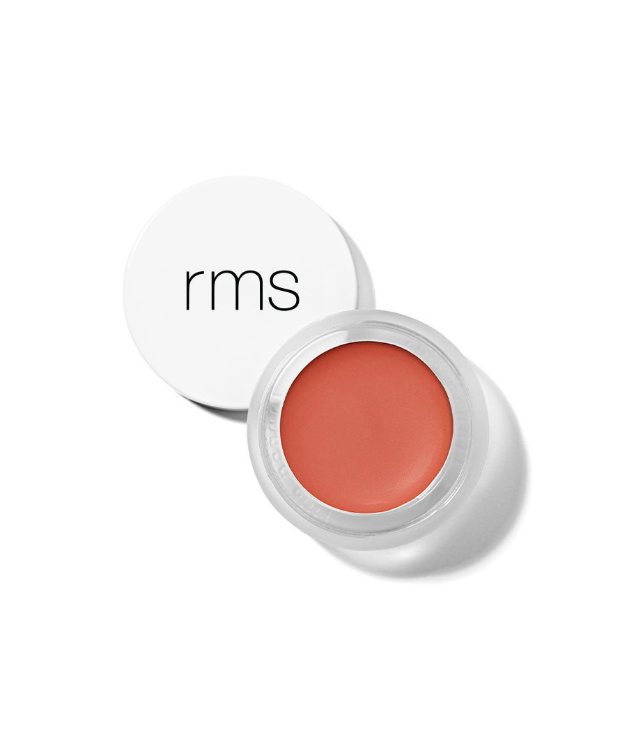 Open container of Lip2Cheek cream makeup in a warm modest coral shade with white lid featuring minimalist black rms branding, showcasing clean beauty and natural ingredients.