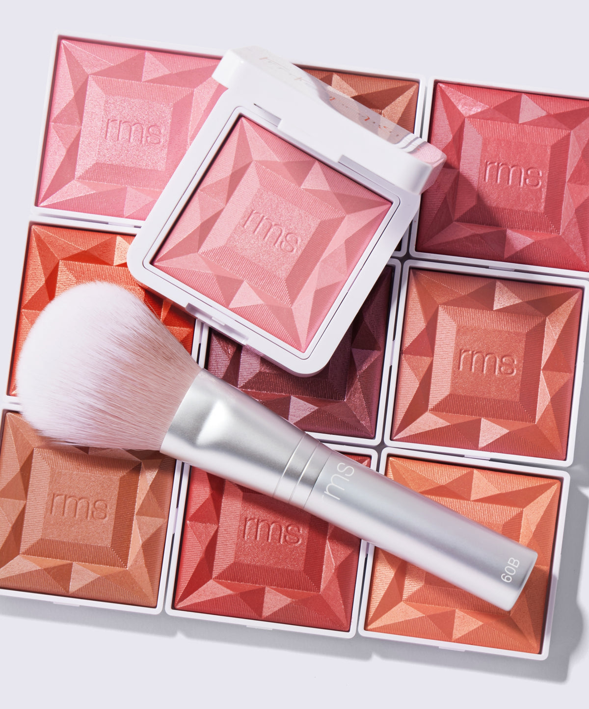 ReDimension Hydra Powder Blush in various warm shades displayed with a soft makeup brush, highlighting clean beauty and skincare infused makeup by RMS Beauty in recyclable packaging.