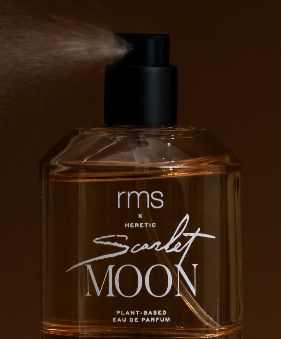 Close-up of a spray bottle releasing mist from RMS x Heretic: Scarlet Moon Fragrance, a plant-based eau de parfum with a sleek black spray nozzle against a dark background.