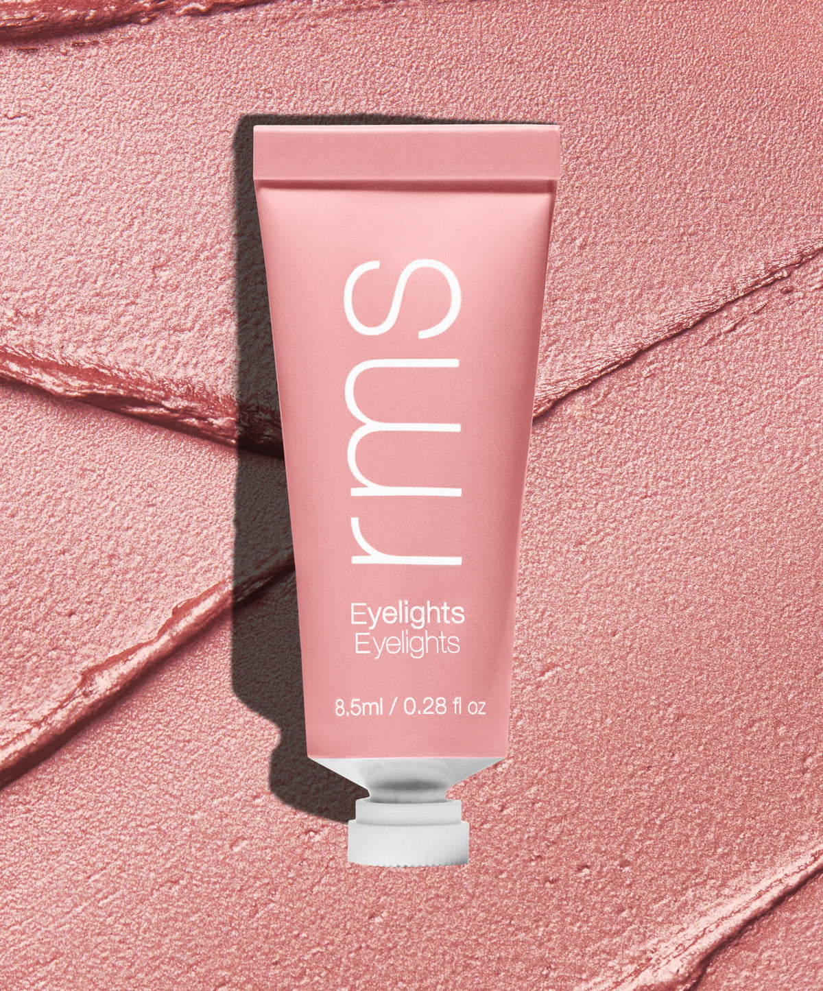 Tube of Eyelights Cream Eyeshadow in a soft, shimmery rose shade lying on a textured matching pink background, highlighting clean beauty and natural ingredients.