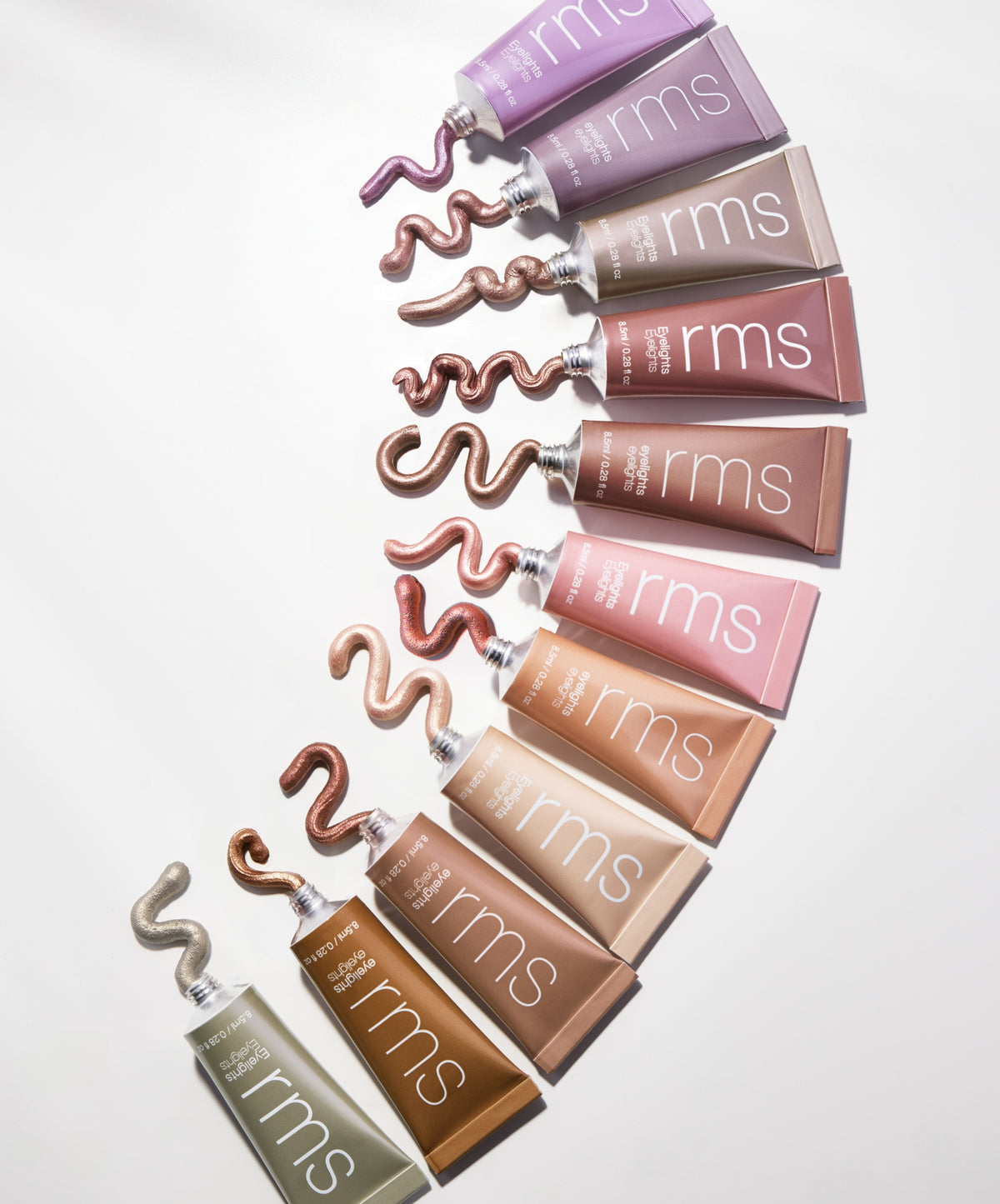 A selection of RMS Beauty Eyelights Cream Eyeshadow tubes arranged in a gradient of shimmering shades, showcasing a variety of natural and radiant colors in recyclable packaging.
