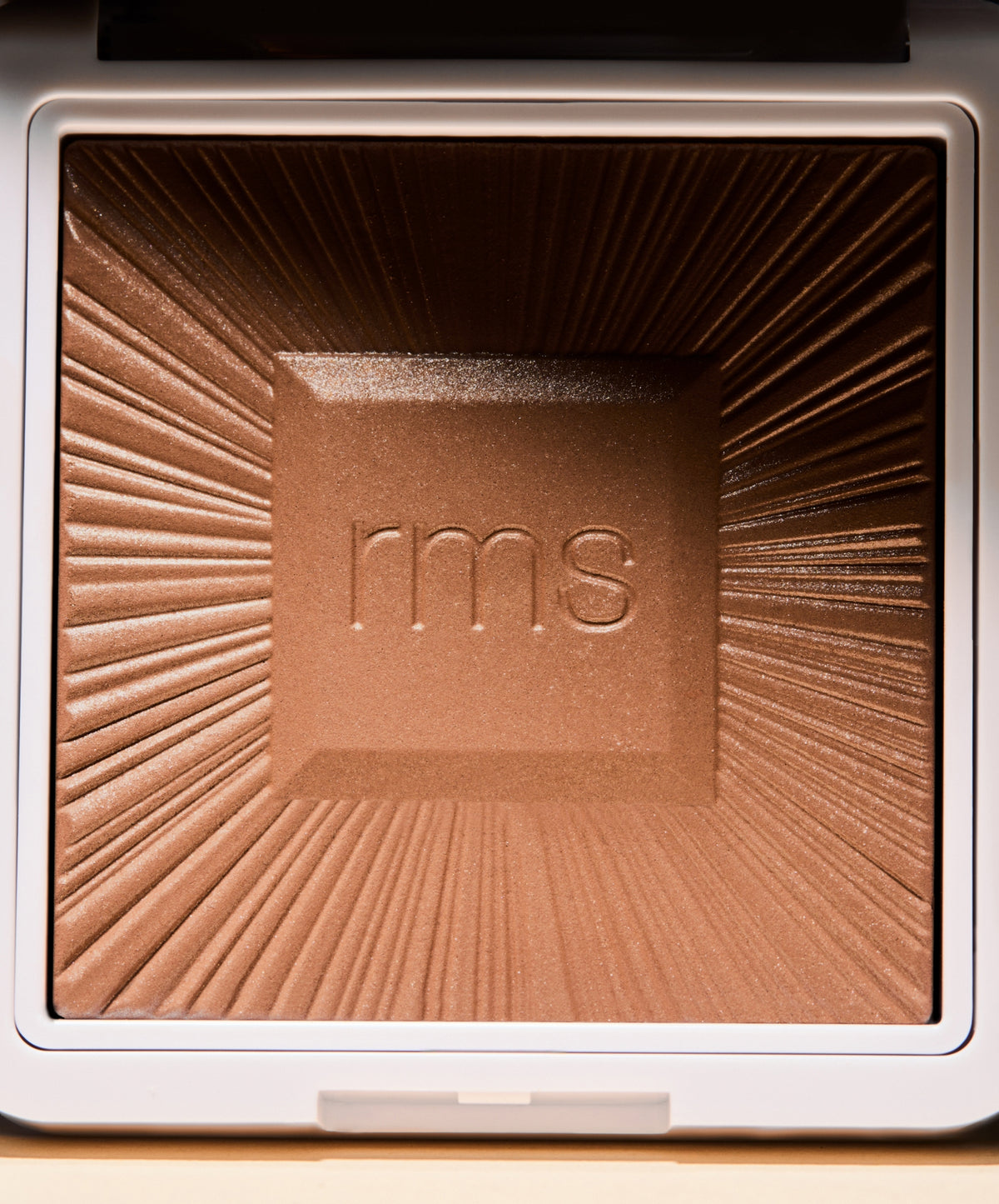 Close-up view of the ReDimension Hydra Bronzer powder with embossed rms logo, showcasing a warm bronzed shade and radiant finish in recyclable packaging.