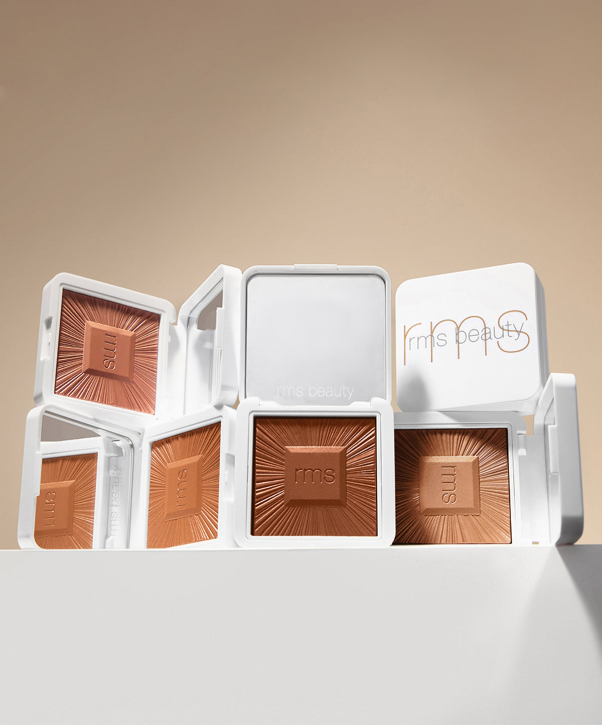 Open white compacts of ReDimension Hydra Bronzer showcasing rich, warm brown shades with embossed rays and rms beauty branding on a neutral background.