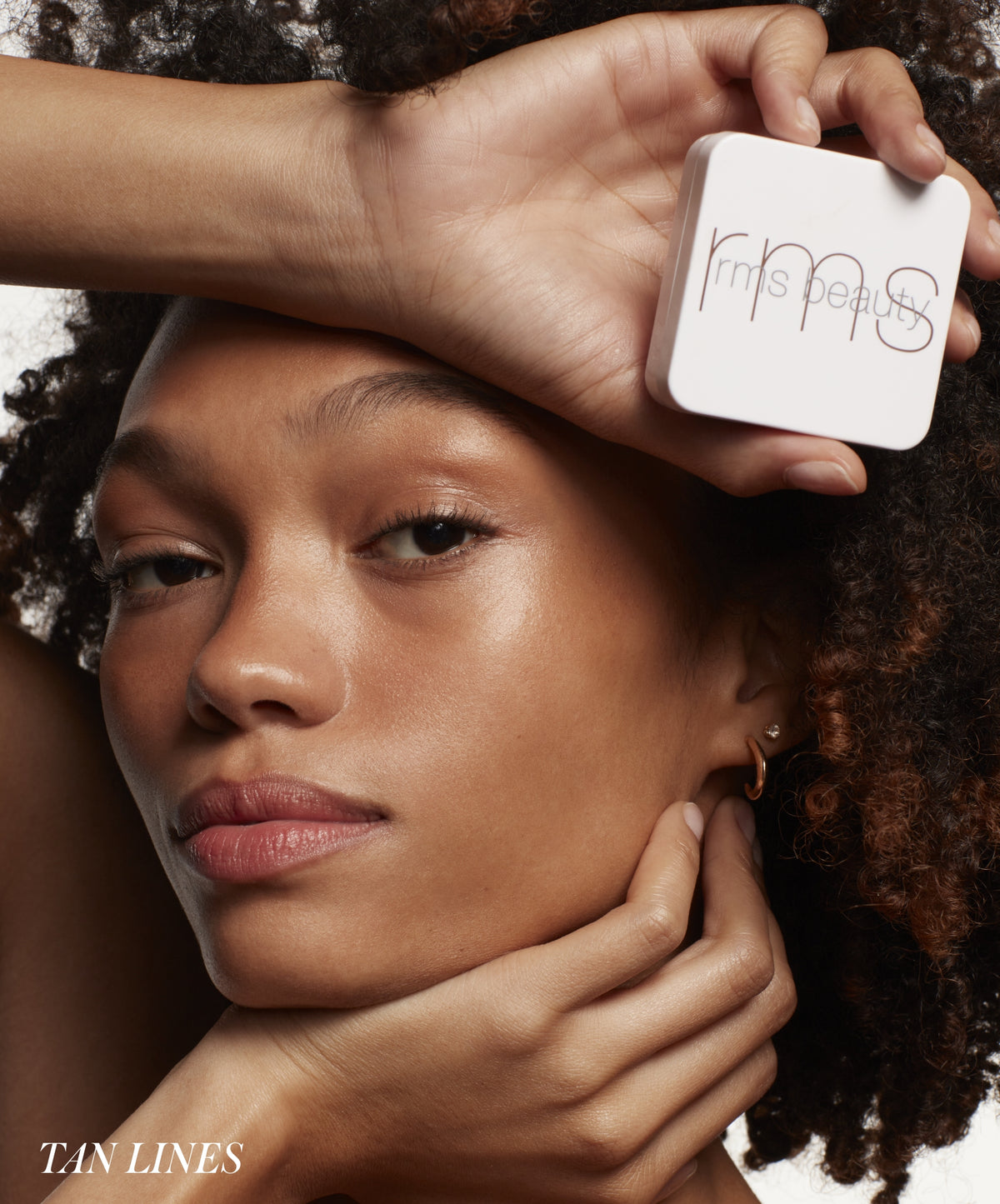 Close-up of a woman with glowing skin holding RMS Beauty ReDimension Hydra Bronzer near her forehead, showcasing natural makeup and radiant complexion.