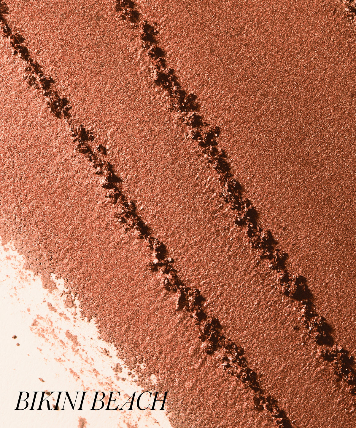 Close-up texture of warm bronze powder makeup with shimmering finish labeled Bikini Beach, showcasing ReDimension Hydra Bronzer in a natural sun-kissed tone.