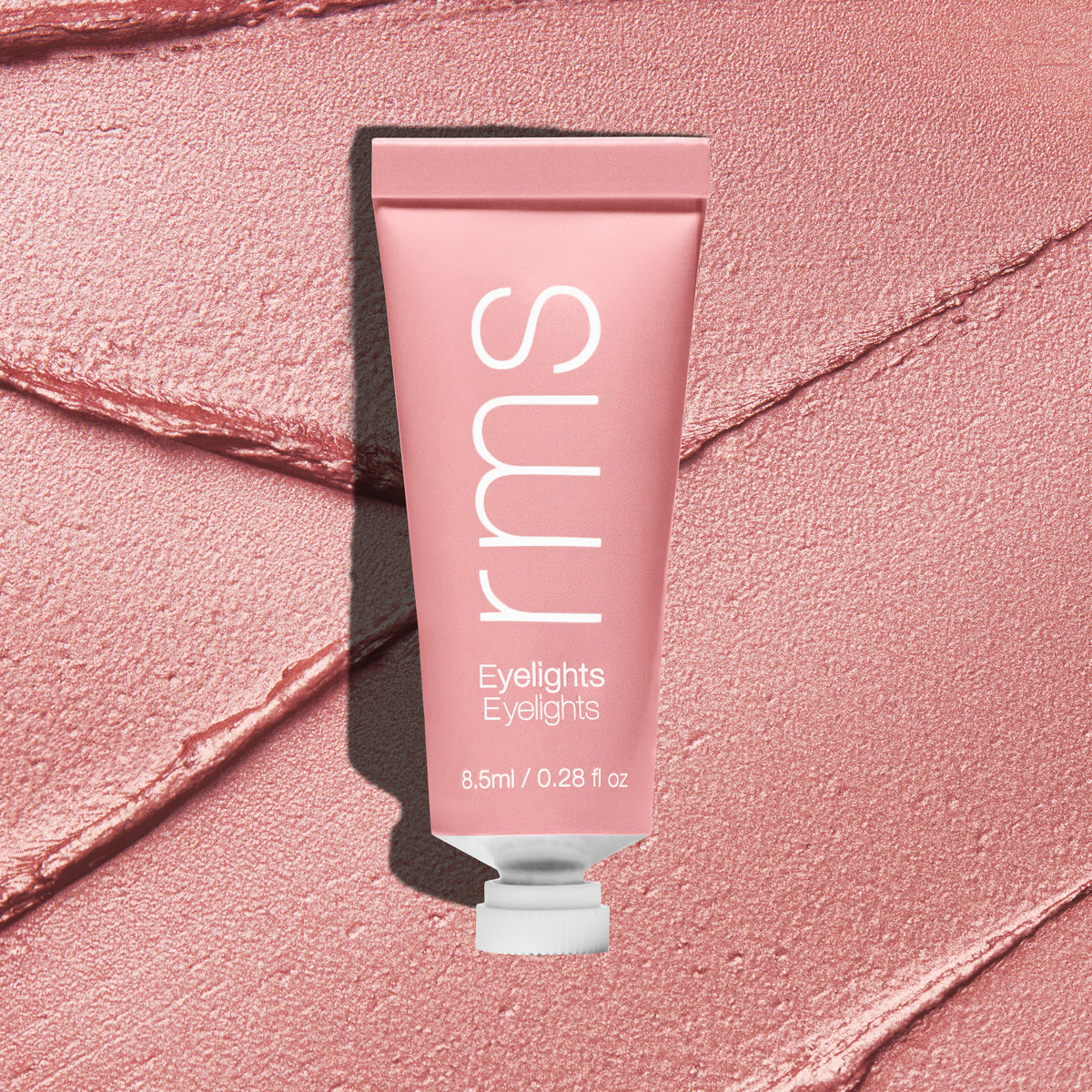Tube of Eyelights Cream Eyeshadow in soft pink shade placed on textured matching cream eyeshadow background, highlighting its smooth, creamy formula and clean beauty appeal.