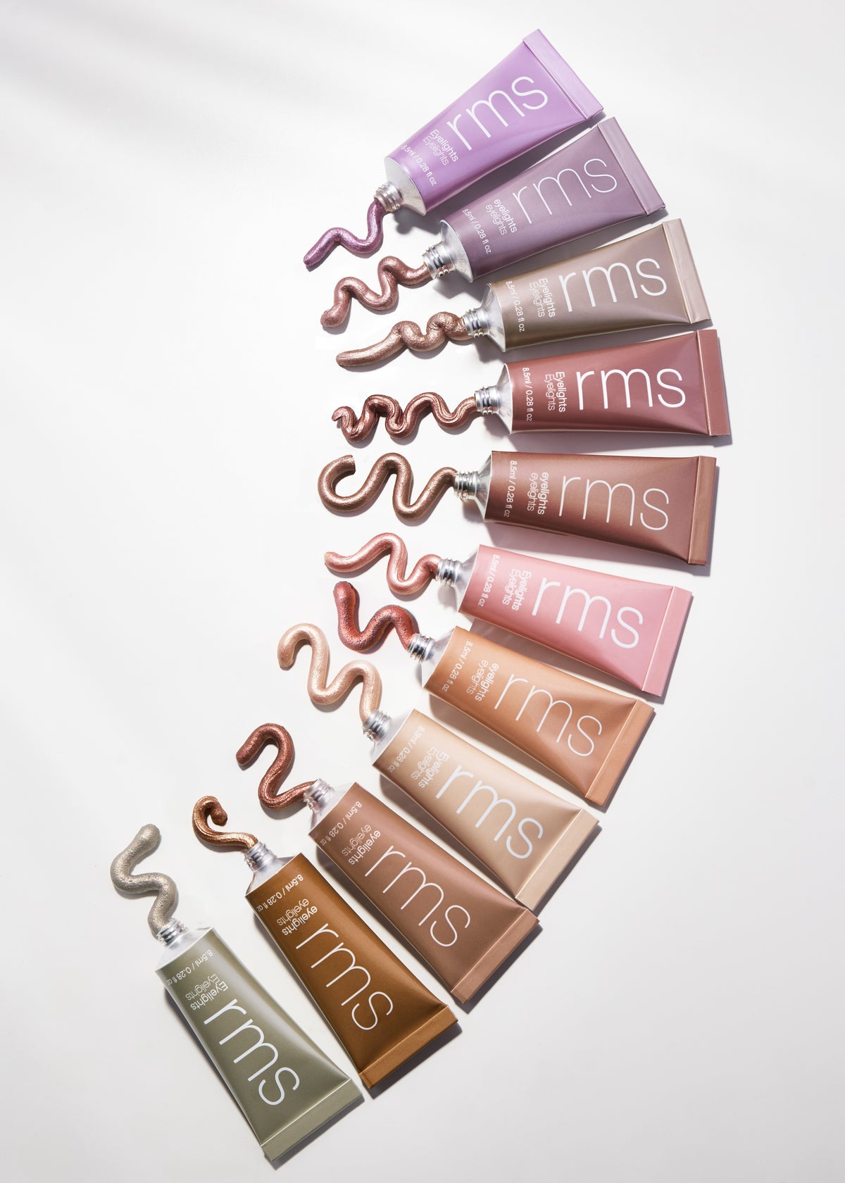 A selection of tubes with various shades of RMS Beauty Eyelights Cream Eyeshadow, each with a swirled cream eyeshadow sample extending from the tube, showcasing a range of natural and metallic colors.