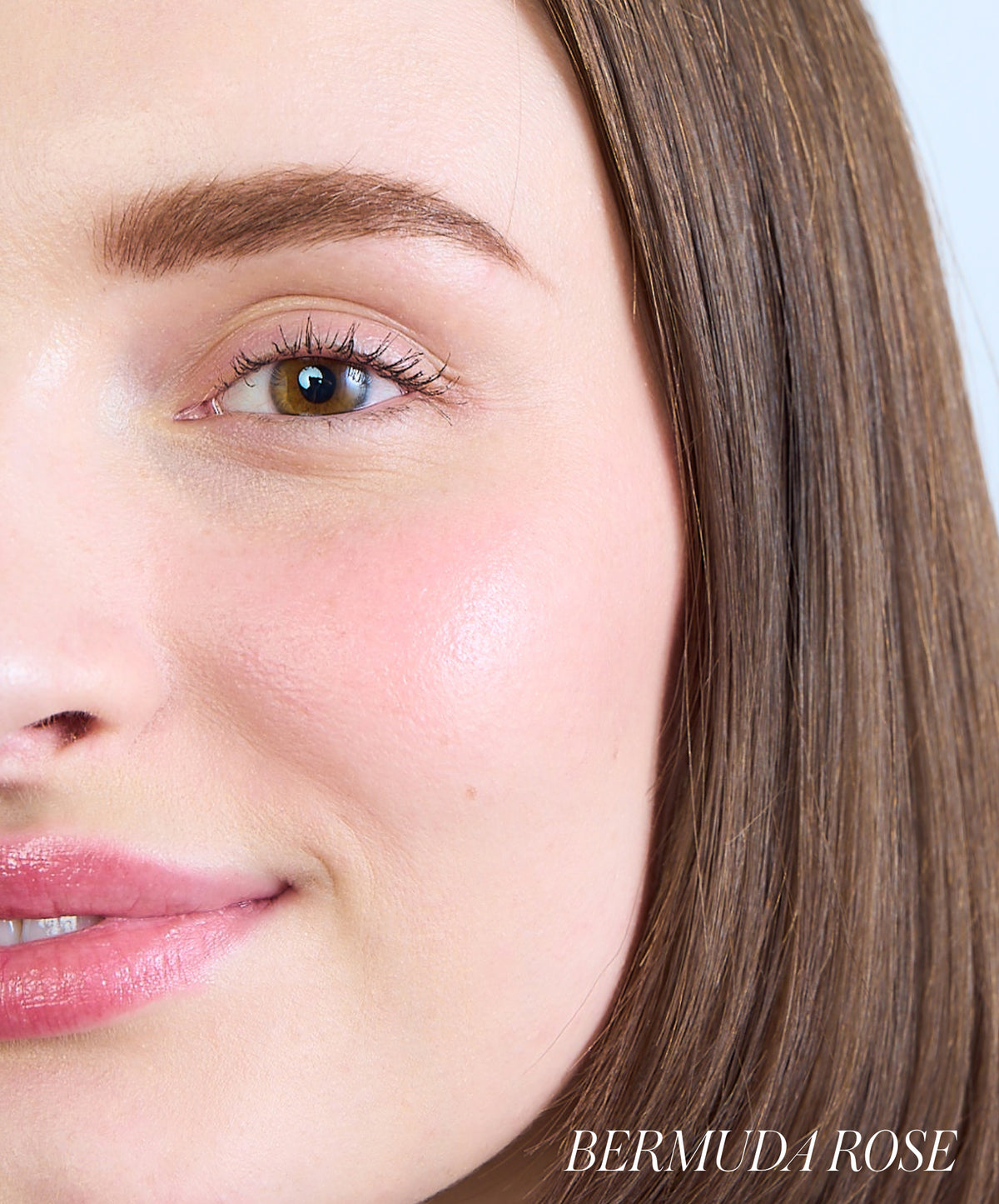 Close-up of a smiling woman with natural skin and subtle rosy cheeks wearing ReDimension Hydra Powder Blush in a soft Bermuda Rose shade, showcasing a clean beauty look.