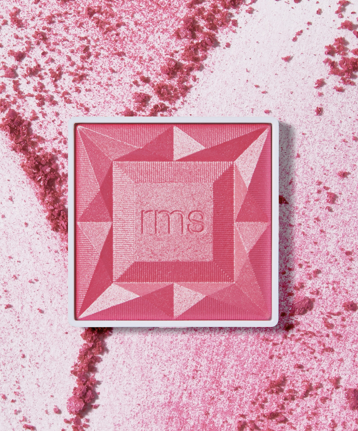 Square compact of ReDimension Hydra Powder Blush in a vibrant pink shade with geometric embossed design and RMS branding, surrounded by crushed powder on a light background.