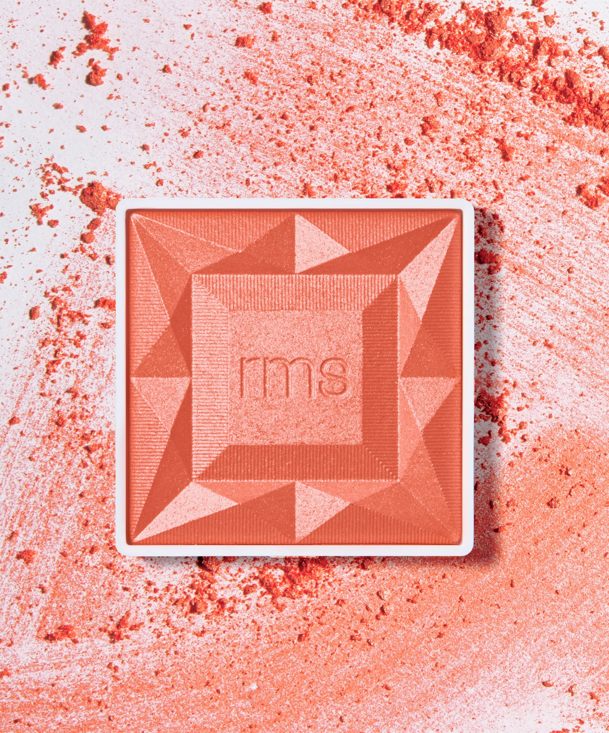 Square compact of ReDimension Hydra Powder Blush in coral shade with geometric embossed pattern and scattered powder on white surface, showcasing clean beauty makeup.