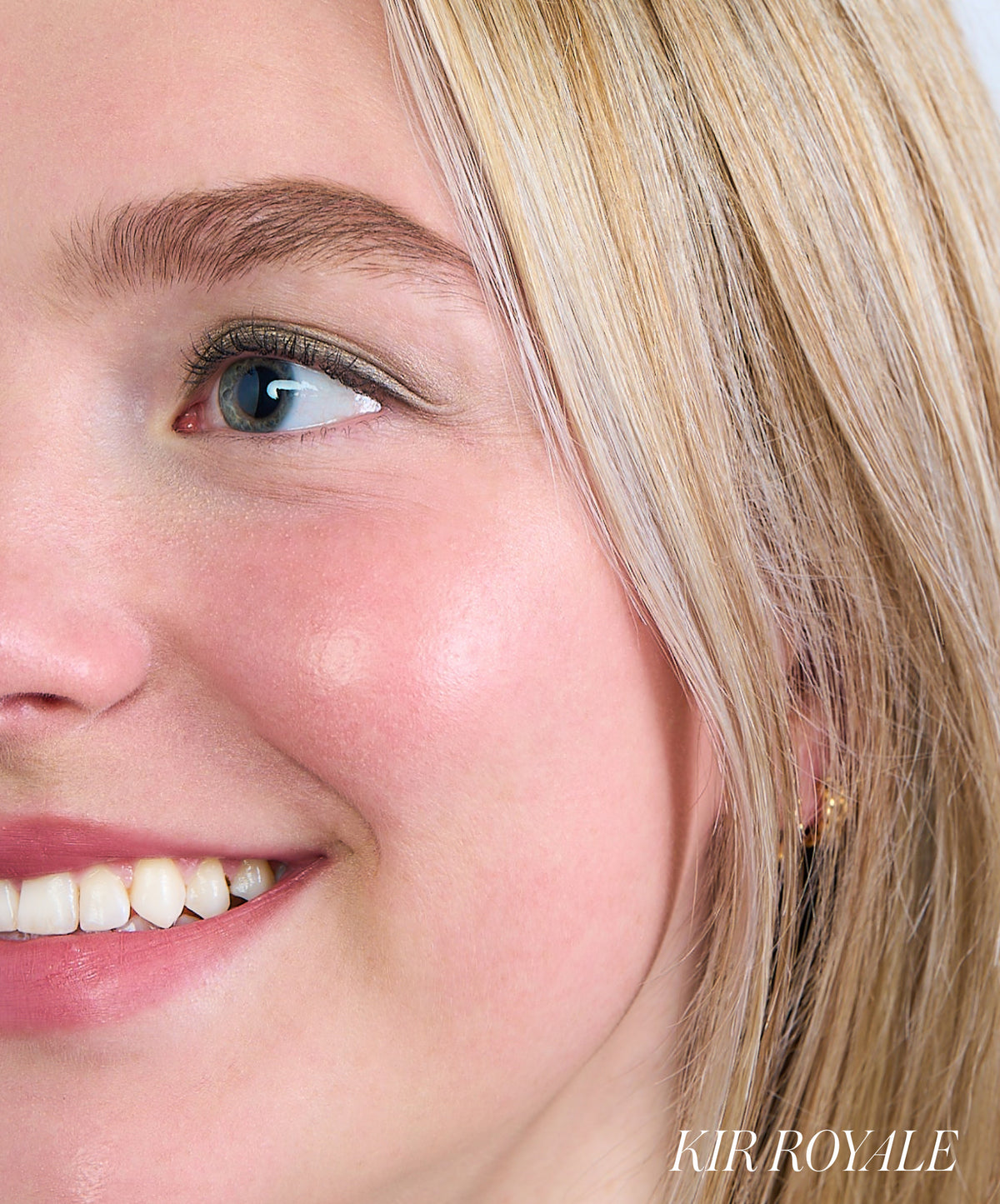 Close-up of a smiling woman with blonde hair showcasing a natural rosy glow on her cheek using ReDimension Hydra Powder Blush for a fresh, clean beauty look.