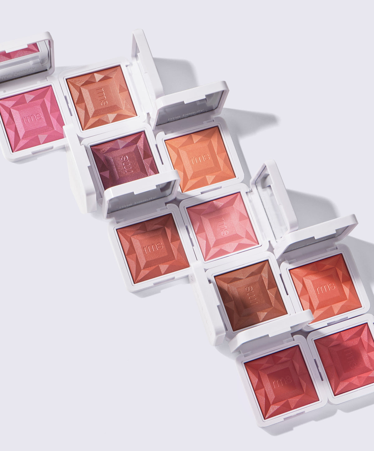 Open compacts of ReDimension Hydra Powder Blush in various warm and rosy shades arranged diagonally on a light background, showcasing clean beauty makeup with natural and sustainable appeal.