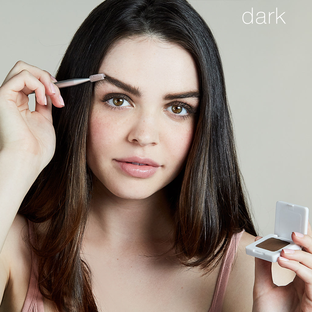 Model using Back2Brow Brush on right brow, holding Back2Brow Powder shade Dark in left hand.