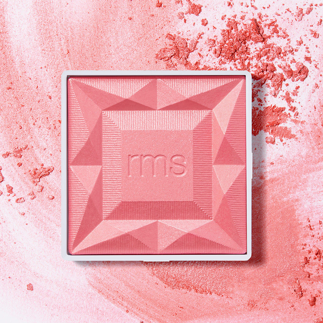 Square compact of ReDimension Hydra Powder Blush in a soft rosy pink shade with geometric embossed design and crushed powder scattered around on a light background