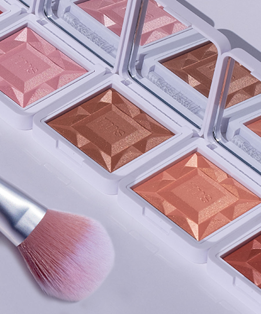 ReDimension Hydra Powder Blush in multiple shades with a geometric pattern in white compact cases, accompanied by a soft pink-tipped makeup brush, showcasing clean beauty and sustainable packaging.