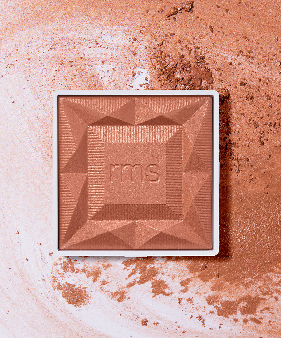 ReDimension Hydra Powder Blush in a warm, earthy tone with a geometric embossed design, surrounded by loose powder on a light background, showcasing clean beauty and natural ingredients.