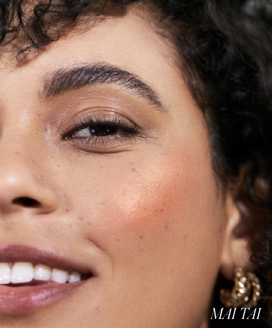Close-up of a smiling woman's face showcasing natural makeup with a warm coral-orange hue on her cheeks using ReDimension Hydra Powder Blush, highlighting clean and radiant skin.