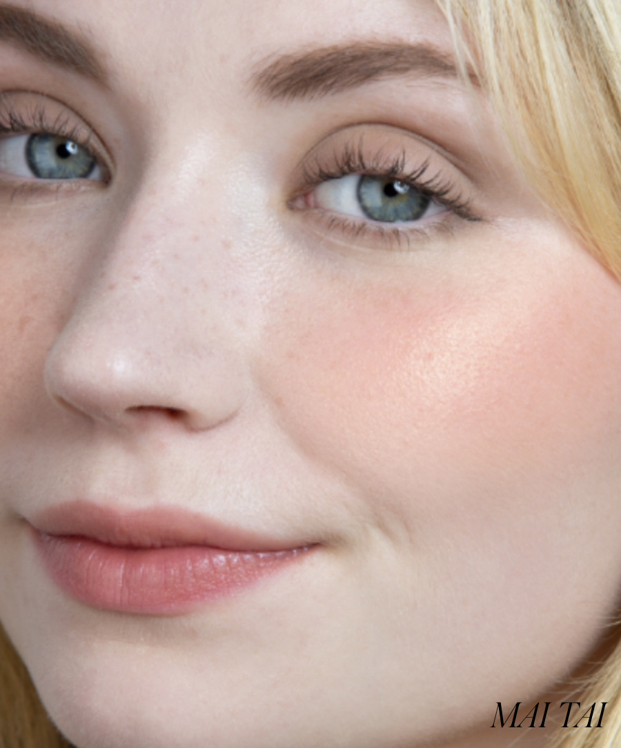 Close-up of a fair-skinned woman with blue eyes wearing ReDimension Hydra Powder Blush in a soft natural peach shade, highlighting glowing, radiant skin with clean beauty makeup.