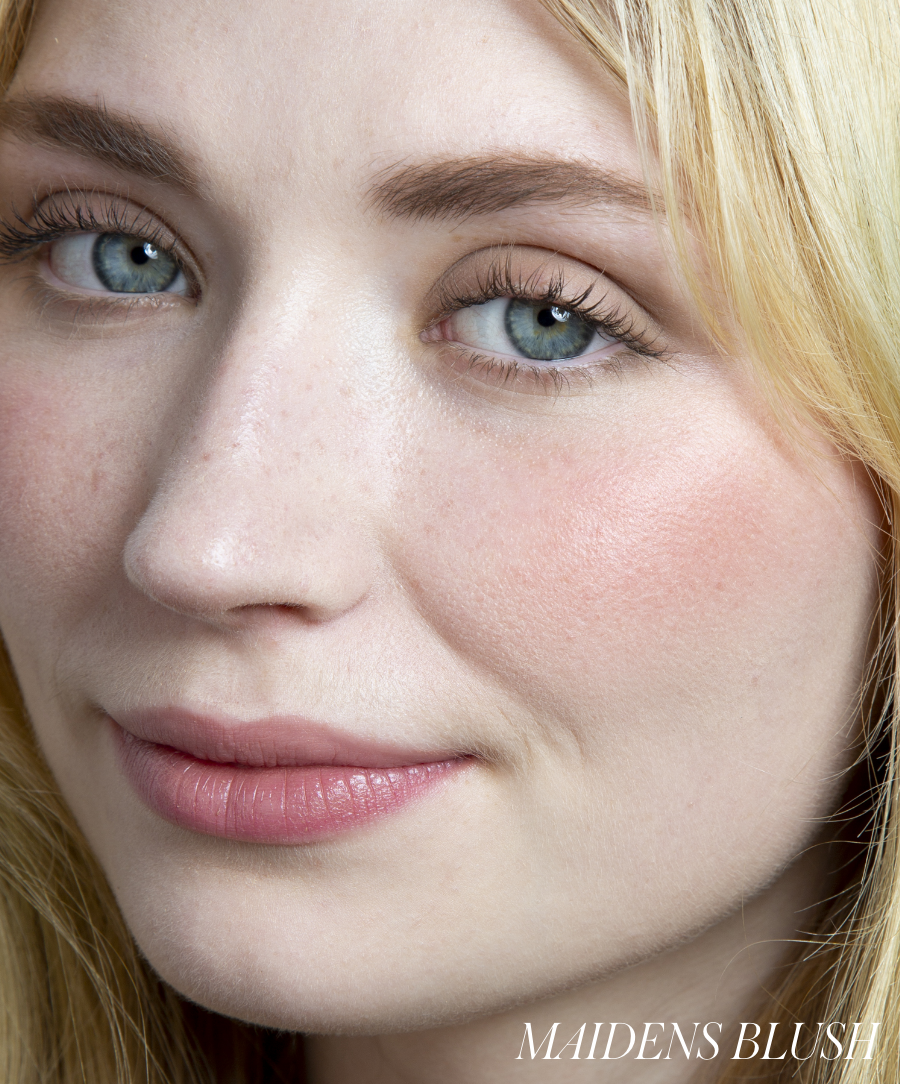 Close-up of a woman with fair skin and blue eyes wearing natural makeup featuring a soft pink glow on her cheeks using ReDimension Hydra Powder Blush, highlighting clean beauty and natural ingredients.