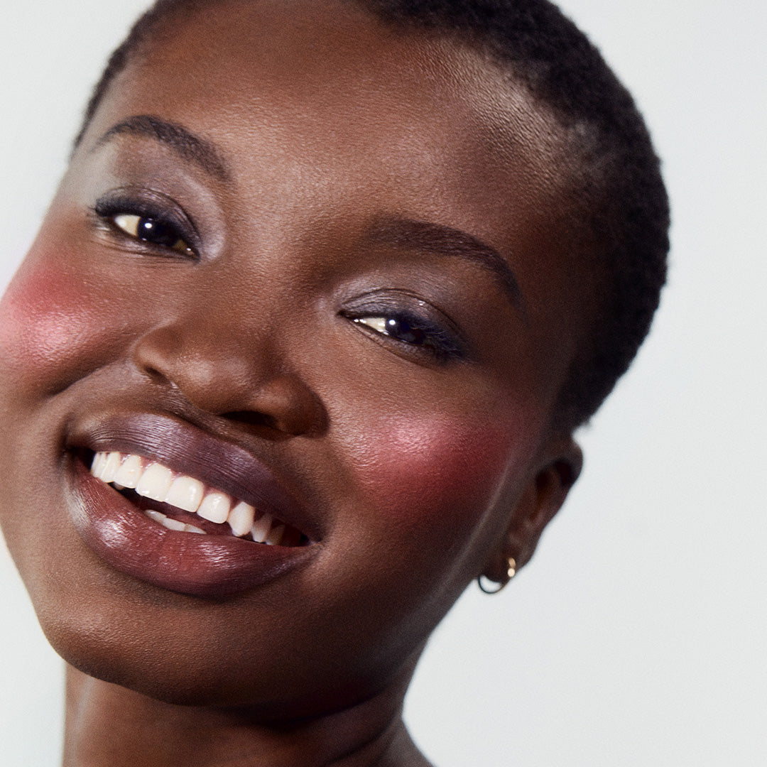 Close-up of a smiling woman with radiant skin wearing ReDimension Hydra Powder Blush in a vibrant shade, highlighting clean beauty and natural ingredients.