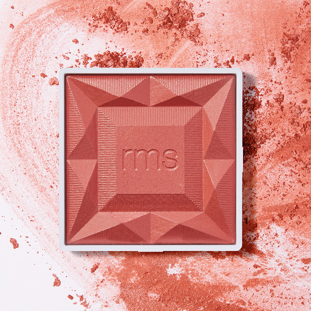 Square compact of ReDimension Hydra Powder Blush in a warm sangria shade with geometric embossed design, surrounded by a soft dusting of blush powder, highlighting clean beauty and natural ingredients.